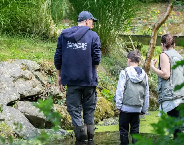 Un soigneur explique son travail à un enfant et un adulte au bord d'un enclos