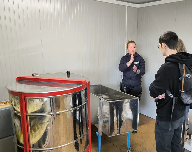 Salle d'extraction du miel avec extracteur en inox et deux personnes en discussion