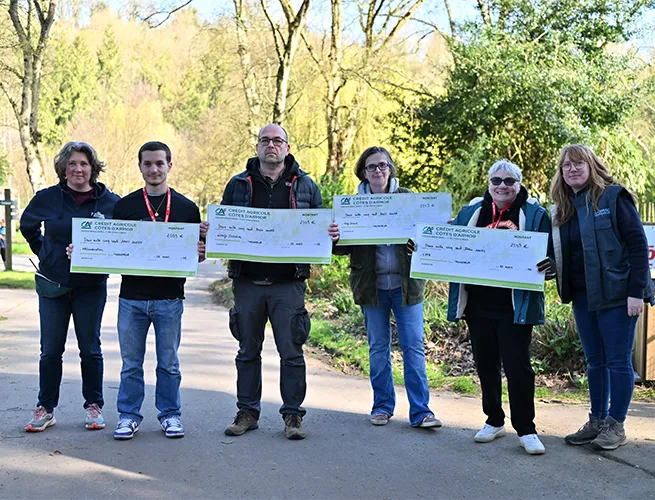Groupe de personnes présentant des chèques géants de dons sur un chemin du parc