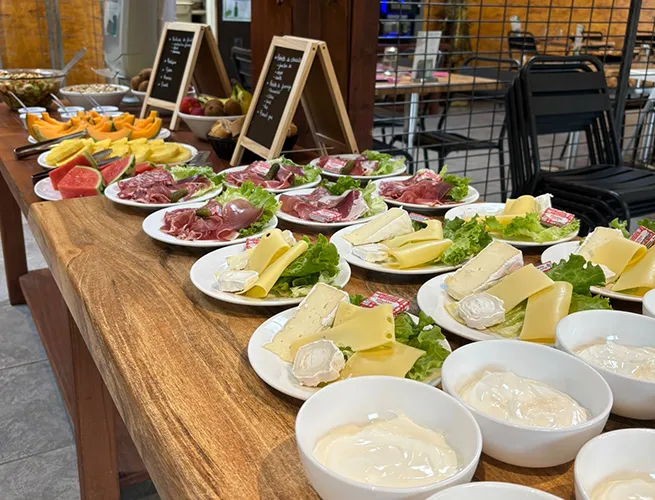 Buffet du brunch dominical : assiettes de charcuterie, fromages, fruits et fromage blanc sur une table en bois