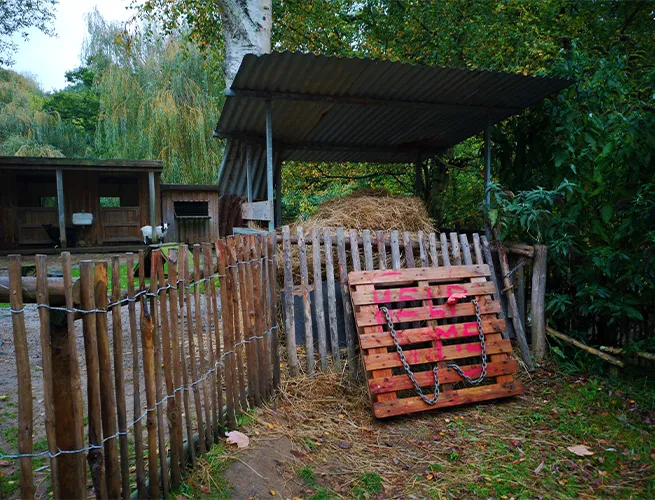 Enclos animalier décoré pour Halloween, avec palissade en bois et palette rouge sous un abri