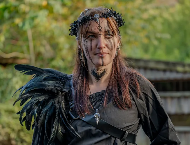 Femme maquillée portant une couronne de feuilles et des ailes noires, déguisée pour Halloween