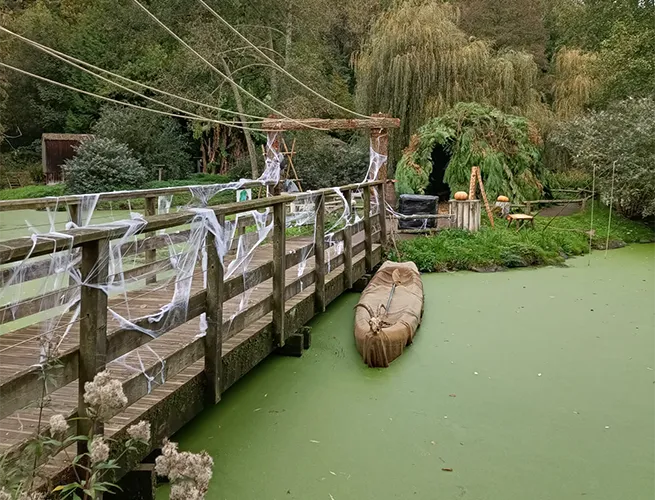 Passerelle en bois ornée de fausses toiles d'araignée au-dessus d'un étang couvert de lentilles d'eau