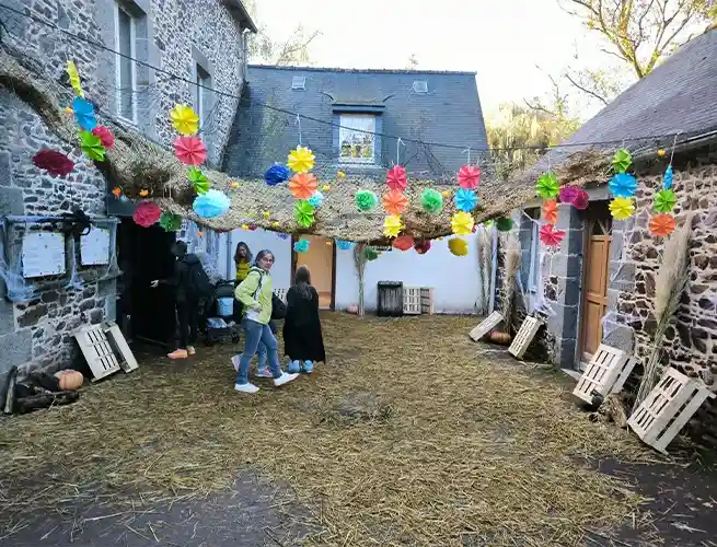 Cour en pierre décorée de guirlandes colorées et de paille pour Halloween, avec quelques visiteurs