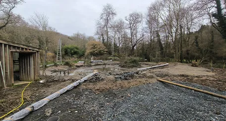 Chantier de la future volière : terrain dégagé avec graviers, planches et bâtiment en bois