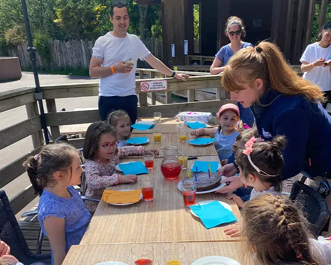 Enfants attablés sur une terrasse en bois pour un goûter d'anniversaire avec des animateurs