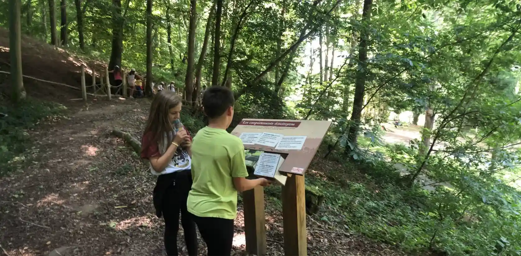 Two children reading an educational panel along a wooded path at the ZooParc de Trégoмeur