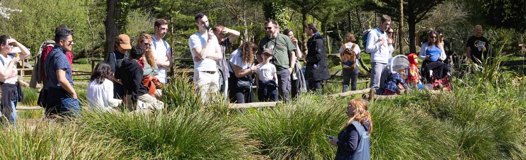 Visiteurs rassemblés au bord d'un étang et d'herbes hautes, une soigneuse dans l'eau en bottes